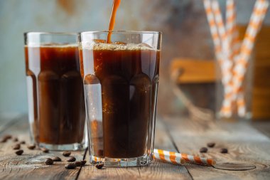 Uzun bir bardak kahve üzerine döktü krem, kahve buz küpleri ile eski rustik ahşap masa fasulyeli buz. Soğuk Yaz içeceği paslı mavi bir arka plan üzerine boruları ile