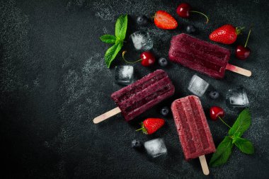 Koyu bir beton arka planda kiraz, çilek ve yaban mersini yapılmış parlak dondurma. Tatlı yaz ikramları. Kopya alanı ile üst görünüm. Düz yatma
