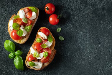 Bruschetta domates, mozzarella peynir ve fesleğen karanlık bir arka planda. Geleneksel İtalyan meze veya aperatifler, antipasto. Kopya alanı ile üst görünüm. Düz yatma