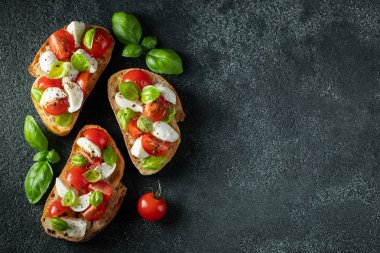 Bruschetta domates, mozzarella peynir ve fesleğen karanlık bir arka planda. Geleneksel İtalyan meze veya aperatifler, antipasto. Kopya alanı ile üst görünüm. Düz yatma