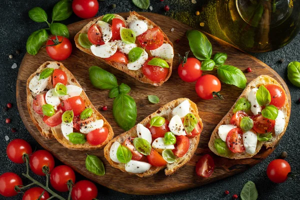 Bruschetta com tomates, queijo mussarela e manjericão em uma tábua de corte. Aperitivo italiano tradicional ou lanche, antipasto. Vista superior com espaço de cópia. Depósito plano — Fotografia de Stock