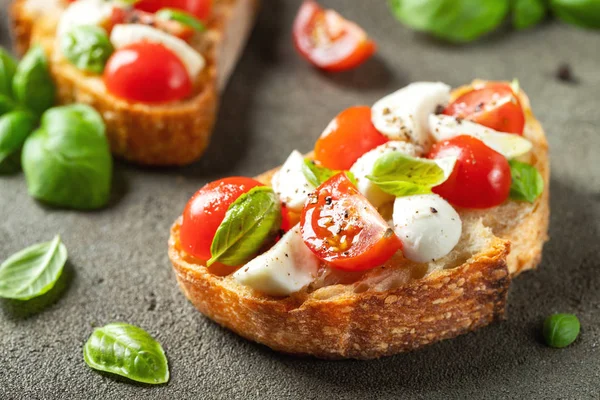 Bruschetta con tomates, queso mozzarella y albahaca sobre una vieja mesa rústica. Aperitivo o merienda tradicional italiana, antipasto —  Fotos de Stock