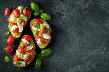 Bruschetta domates, mozzarella peynir ve fesleğen karanlık bir arka planda. Geleneksel İtalyan meze veya aperatifler, antipasto. Kopya alanı ile üst görünüm. Düz yatma
