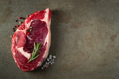 Kahverengi beton arka plan üzerinde otlar ve baharatlar ile Çiğ ribeye sığır biftek. Üst te. Düz yatıyordu.