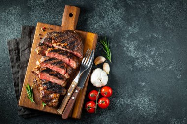 Dilimlenmiş biftek ribeye, biber, sarımsak, tuz ve kekik ile ızgara koyu taş arka plan üzerinde ahşap kesme Kurulu servis. Üst te. Düz yatıyordu