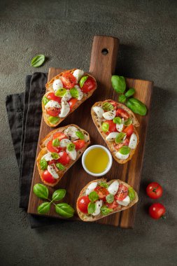 Bruschetta domates, mozzarella peyniri ve fesleğen bir kesme tahtası üzerinde. Geleneksel İtalyan meze veya aperatif, meze. Üstten görünüm. Düz yatıyordu