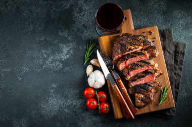 Dilimlenmiş biftek ribeye, biber ile ızgara, sarımsak, tuz ve keklik koyu taş arka planda bir tahta kesme kurulu üzerinde hizmet. Kopya alanı ile üst görünüm. Düz yatma
