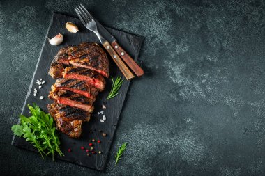Dilimlenmiş biftek ribeye, biber ile ızgara, sarımsak, tuz ve keklik koyu taş arka planda bir arduvaz kesme kurulu üzerinde hizmet. Kopya alanı ile üst görünüm. Düz yatma