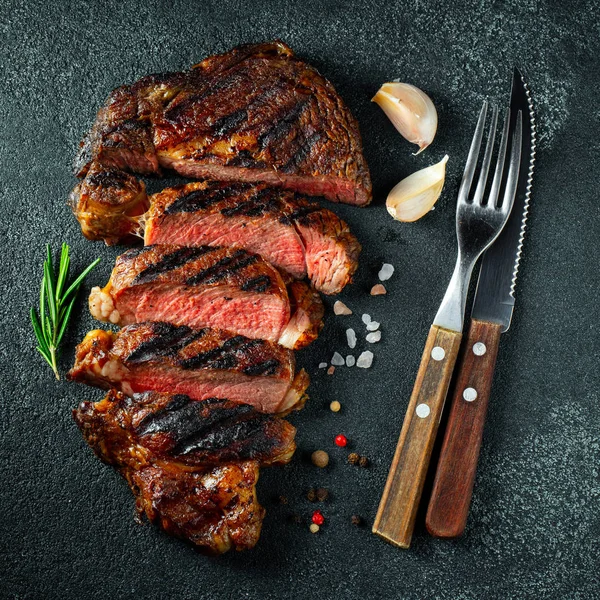 Bistecca affettata ribeye, alla griglia con pepe, aglio, sale e timo su uno sfondo di pietra scura. Vista dall'alto. Posa piatta — Foto Stock