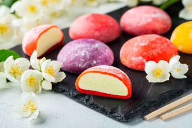 Çok renkli Japon dondurma mochi pirinç hamur ve yasemin çiçekler somut bir mavi arka planda. Siyah bir arduvaz üzerinde geleneksel Japon tatlı