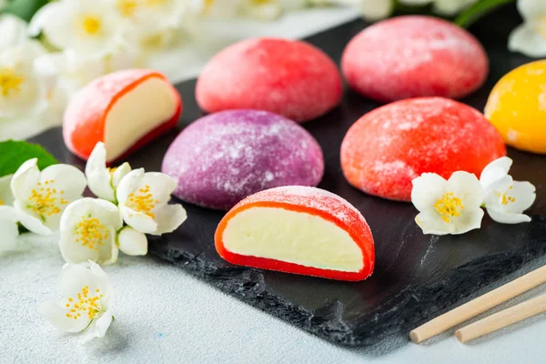 Çok renkli Japon dondurma mochi pirinç hamur ve yasemin çiçekler somut bir mavi arka planda. Siyah bir arduvaz üzerinde geleneksel Japon tatlı