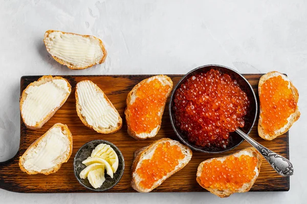 Close-up red caviar in bowl and Sandwiches on wooden cutting board on white background. Top view with copy space. Flat lay — Stock Photo, Image