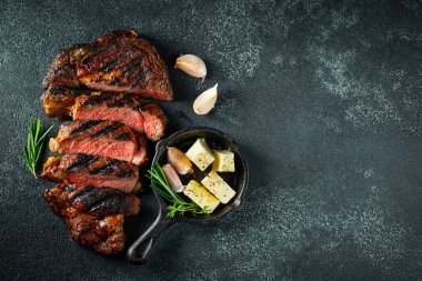 Dilimlenmiş biftek ribeye, biber, sarımsak, tuz ve kekik ile ızgara koyu taş arka plan üzerinde. Üst te. Düz yatıyordu