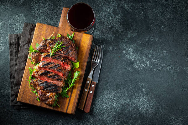 Sliced steak ribeye, grilled with pepper, garlic, salt and thyme served on a wooden cutting Board on a dark stone background. Top view. Flat lay