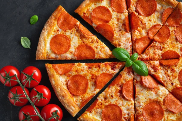 Leckere Pfefferoni-Pizza und Kochzutaten Tomaten Basilikum auf schwarzem Betongrund. Blick von oben auf Chili-Pizza. flache Lage — Stockfoto