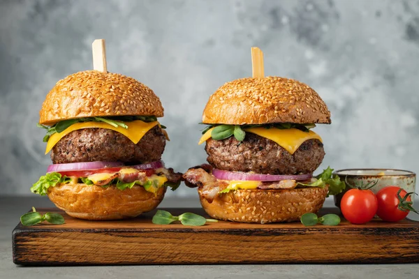 Egy sor házi készítésű finom hamburgert marha, szalonna, sajt, fejes saláta és a paradicsom egy könnyű beton háttér. Kövér egészségtelen élelmiszerek közelről — Stock Fotó