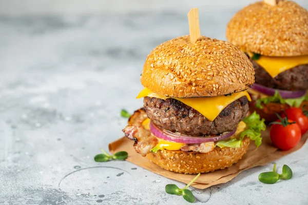 Un conjunto de deliciosas hamburguesas caseras de carne de res, tocino, queso, lechuga y tomates sobre un fondo de hormigón ligero. Comida grasa poco saludable de cerca. Con espacio de copia — Foto de Stock