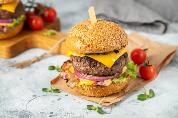 Un conjunto de deliciosas hamburguesas caseras de carne de res, tocino, queso, lechuga y tomates sobre un fondo de hormigón ligero. Comida grasa poco saludable de cerca — Foto de Stock