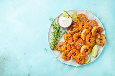 Izgara karides şiş veya langoustines açık mavi beton arka plan üzerinde kireç, sarımsak ve sos ile servis edilir. Deniz ürünleri. Kopyalama alanı ile üst görünüm. Düz yatıyordu