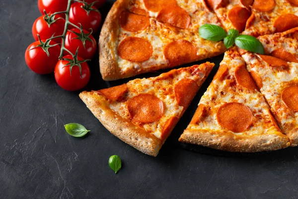 Leckere Pfefferoni-Pizza und Kochzutaten Tomaten Basilikum auf schwarzem Betongrund. Blick von oben auf Chili-Pizza. flache Lage — Stockfoto