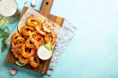 Açık mavi beton zemin üzerinde limon, sarımsak ve sosla servis edilen ızgara karides şişleri veya langoustinler. Deniz ürünleri ve bira. Kopyalama alanı olan üst görünüm. Düz yatıyordu