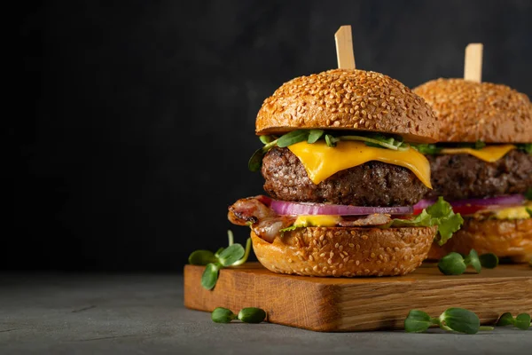 Egy sor házi készítésű finom hamburgert marha, szalonna, sajt, fejes saláta és a paradicsom egy sötét beton háttér. FAT egészségtelen élelmiszer közelről. Másolati hellyel — Stock Fotó
