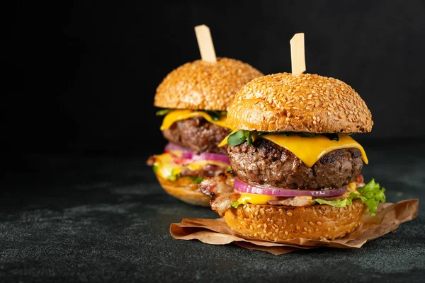 Un conjunto de deliciosas hamburguesas caseras de carne de res, tocino, queso, lechuga y tomates sobre un fondo de hormigón oscuro. Comida grasa poco saludable de cerca. Con espacio de copia — Foto de Stock