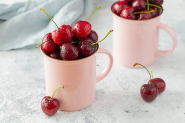 Taze kirazlı iki pembe kupa. Hafif beton arkaplanda tatlı organik meyveler