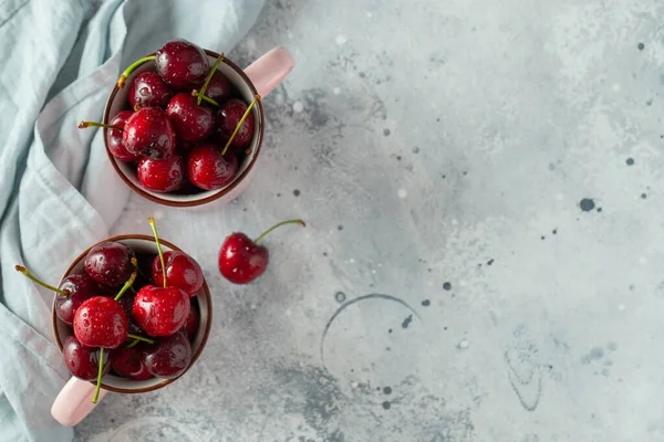 Two pink mugs with fresh ripe cherries. Sweet organic berries on a light concrete background. Top view with copy space — Stock Photo, Image