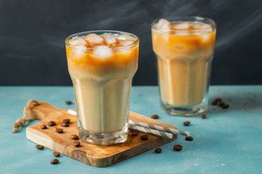 Büyük bardakta buzlu kahve, krema dökülmüş ve kahve çekirdekleri arka planda. Tüplerle soğuk yaz içkisi.