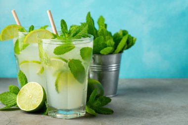 İki ev yapımı limonata ya da mojito kokteyli, limon, nane şekeri ve buz küpleriyle birlikte, hafif taş bir masanın üzerinde. Taze yaz içkisi. Kopyalama alanı ile