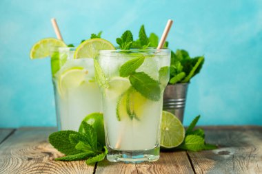 İki ev yapımı limonata ya da mojito kokteyli, limon, nane şekeri ve buz küpleriyle birlikte, hafif taş bir masanın üzerinde. Taze yaz içeceği.