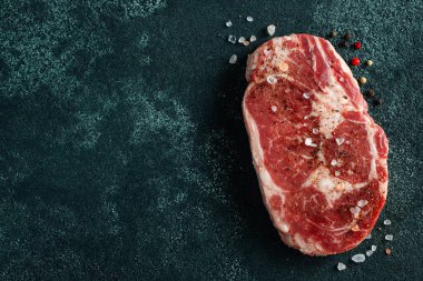 Çiğ et, Ribeye bifteği ve koyu arkaplanda baharat. Kopyalama alanı olan üst görünüm. Düz yatıyordu.
