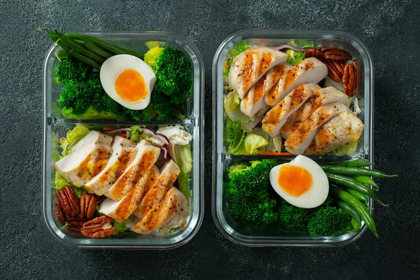 Healthy meal prep containers with green beans, chicken breast and broccoli. A set of food for keto diet in lunchbox on a dark concrete background. Top view.