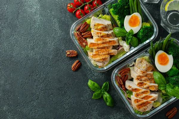 Healthy meal prep containers with green beans, chicken breast and broccoli. A set of food for keto diet in lunchbox on a dark concrete background. Top view with copy space.