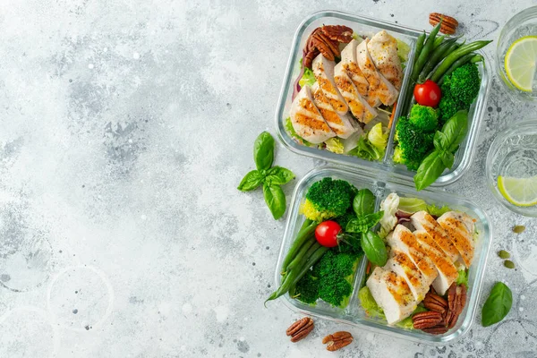 Healthy meal prep containers with green beans, chicken breast and broccoli. A set of food for keto diet in lunchbox on a light concrete background. Top view with copy space.