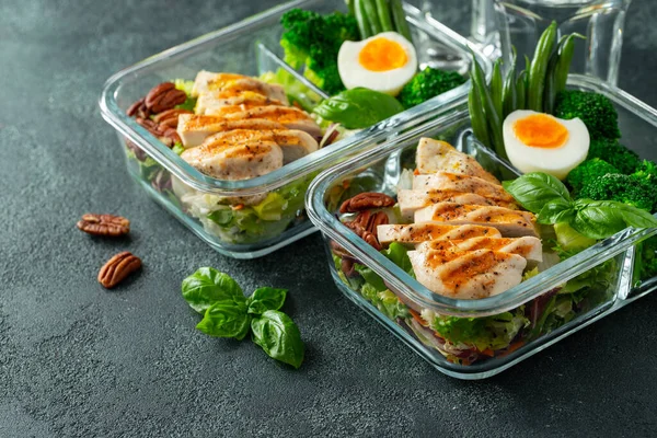 Healthy meal prep containers with green beans, chicken breast and broccoli. A set of food for keto diet in lunchbox on a dark concrete background. Top view.