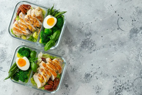 Healthy meal prep containers with green beans, chicken breast and broccoli. A set of food for keto diet in lunchbox on a light concrete background. Top view with copy space