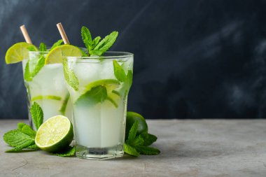 İki ev yapımı limonata ya da limon, nane ve buzlu mojito kokteyli koyu taştan bir masada bir bardakta. Taze yaz içkisi. Kopyalama alanı ile.