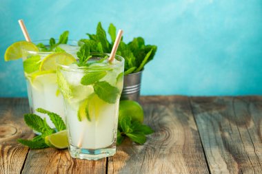İki ev yapımı limonata ya da mojito kokteyli, limon, nane ve buz küpleri ahşap bir kırsal masada bir bardakta. Taze yaz içkisi. Kopyalama alanı ile.