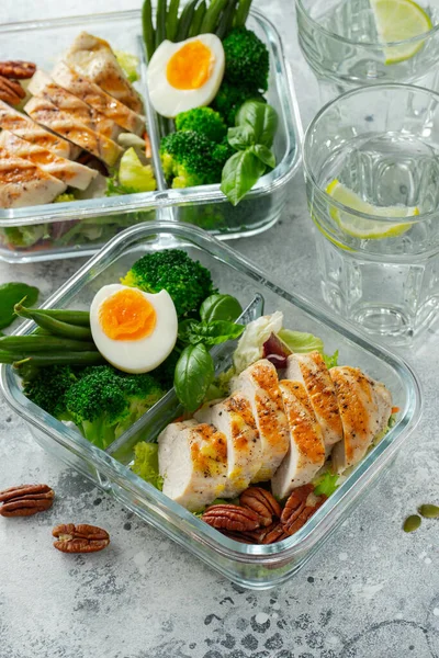 Healthy meal prep containers with green beans, chicken breast and broccoli. A set of food for keto diet in lunchbox on a light concrete background. Top view