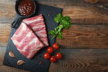 Baharatlı çiğ domuz pirzolası, siyah ahşap arka planda tuz ve biberiye. Kopyalama alanı olan üst görünüm.