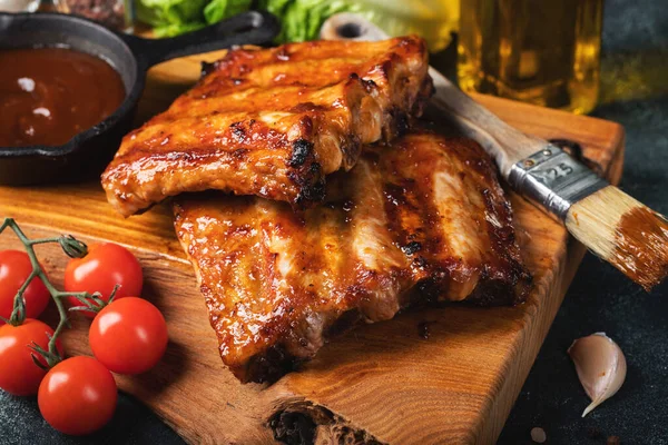 Baharatlı, ızgara pirzola. Barbekü, acı biber ve taze domatesle servis edilir. Eski bir ahşap kesim tahtasının üzerinde.