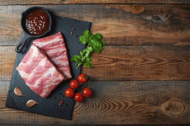 Baharatlı çiğ domuz pirzolası, siyah ahşap arka planda tuz ve biberiye. Kopyalama alanı olan üst görünüm.