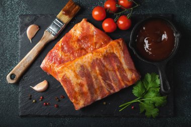 Barbekü, çiğ domuz pirzolası ve barbekü sosu hazır. Siyah arka plan. Üst görünüm.