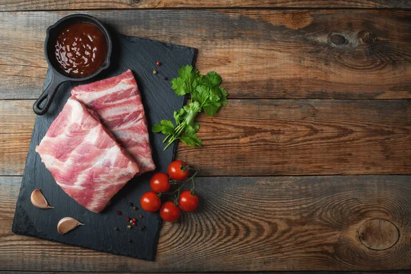 Baharatlı çiğ domuz pirzolası, siyah ahşap arka planda tuz ve biberiye. Kopyalama alanı olan üst görünüm.