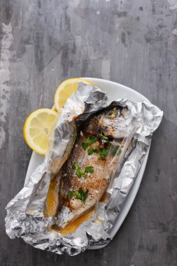 Seramik arka planda alüminyum folyo limon ile pişmiş balık