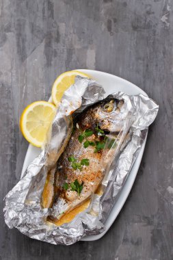 Seramik arka planda alüminyum folyo limon ile pişmiş balık