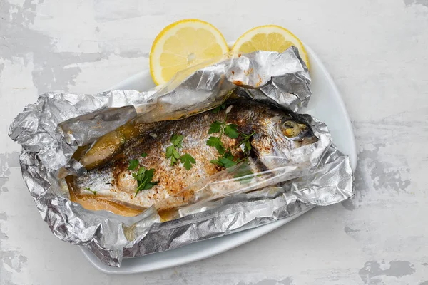 Gebackener Fisch mit Zitrone in Alufolie auf keramischem Hintergrund — Stockfoto