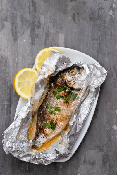 Gebackener Fisch mit Zitrone in Alufolie auf keramischem Hintergrund — Stockfoto